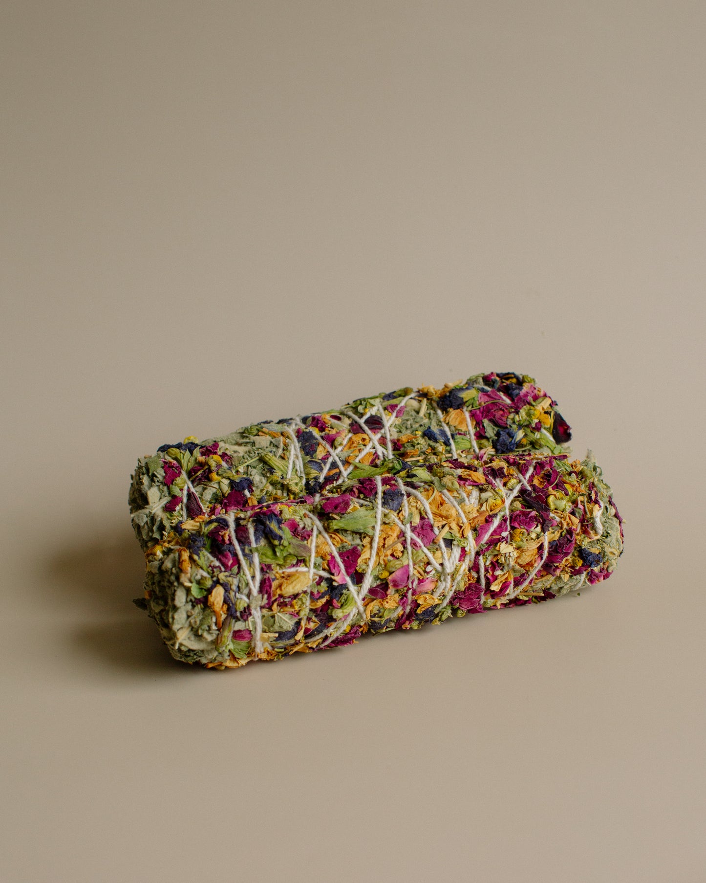 Rolled-up herbal incense with colorful dried flowers on a beige background