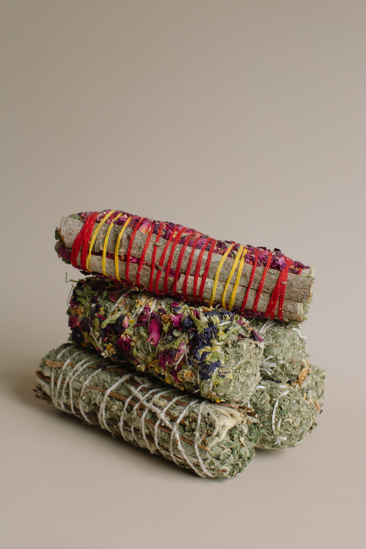 Three bundles of sage wrapped in ribbons stacked on a beige background