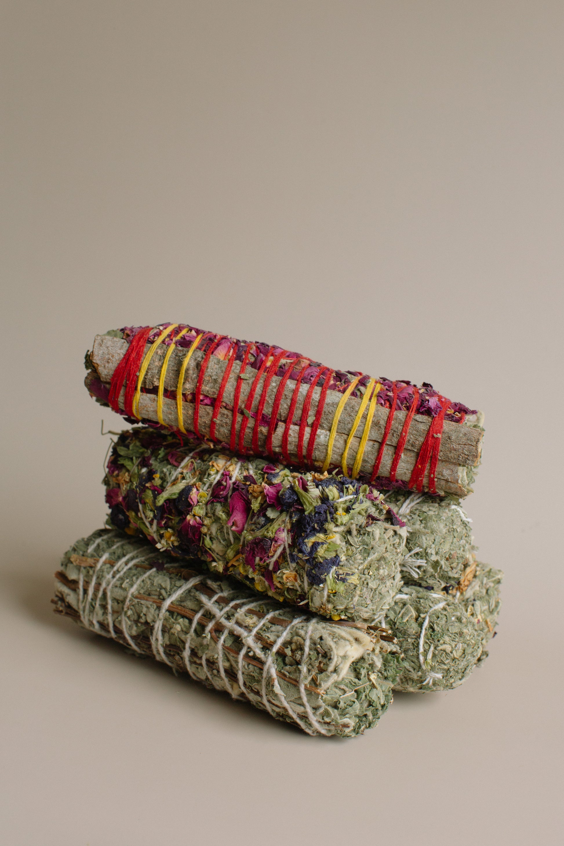 Three bundles of sage wrapped in ribbons stacked on a beige background