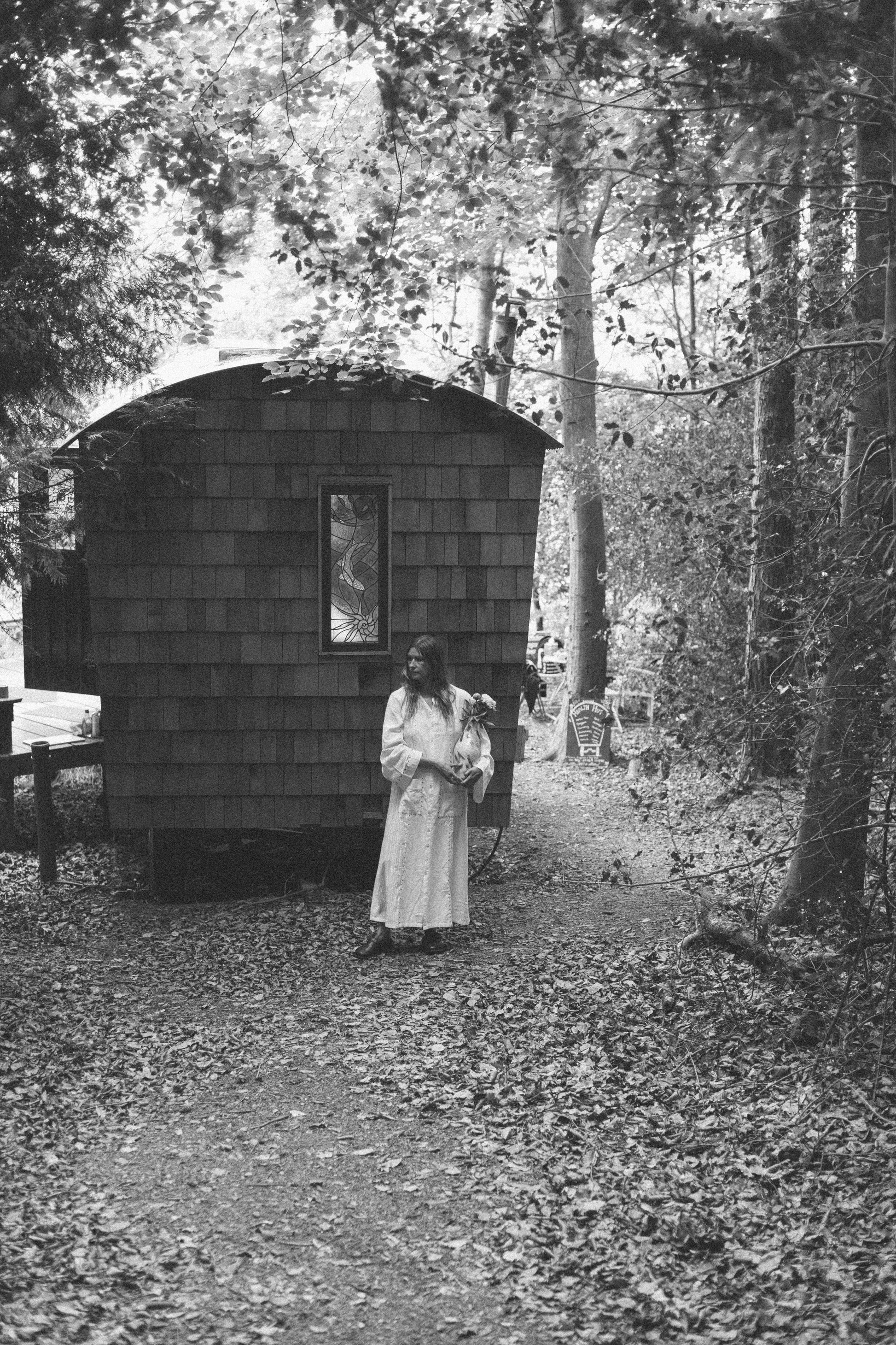 Woman standing in front of a small wooden cabin in a forest setting