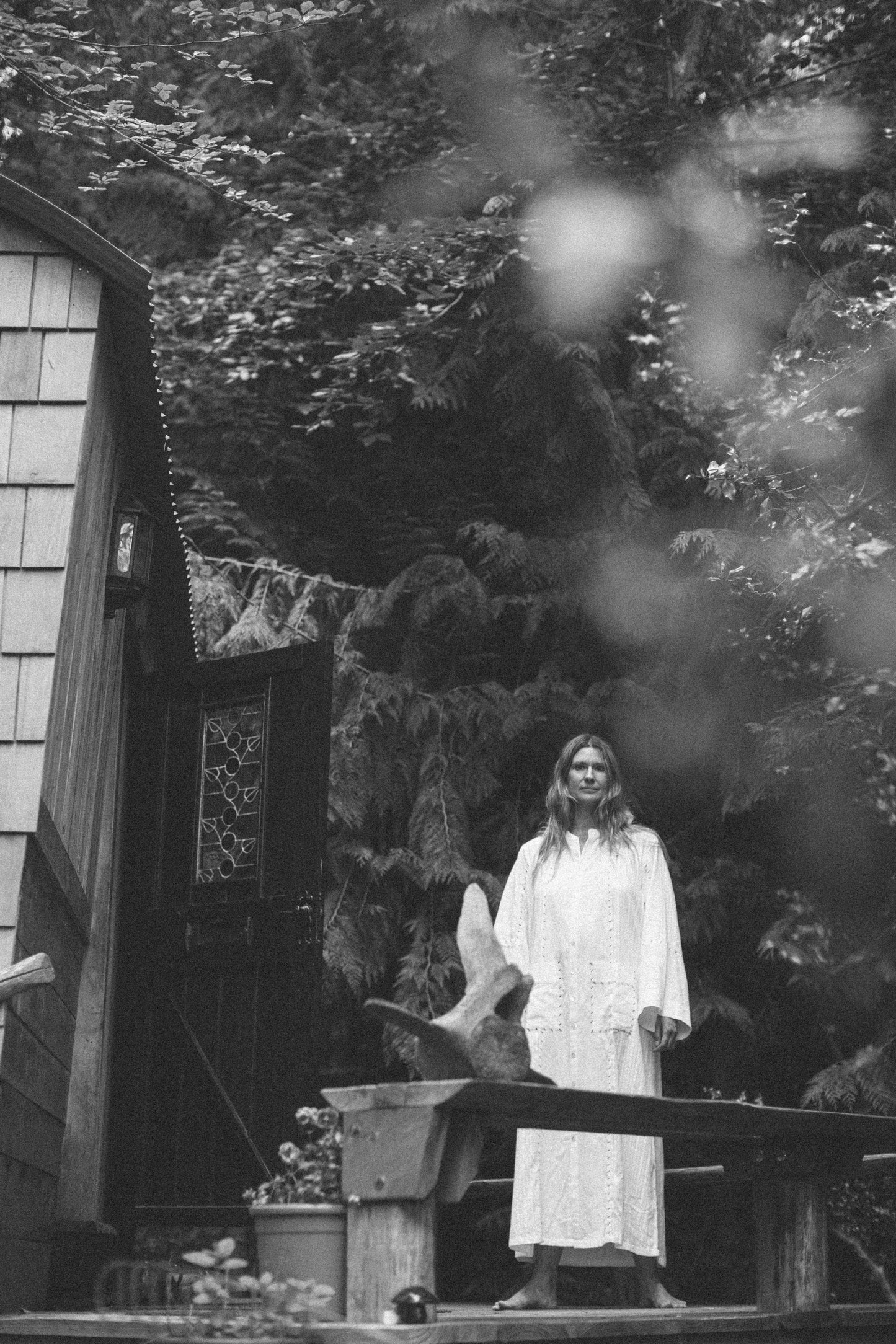 Olivia in a white dress standing on a wooden deck with trees in the background