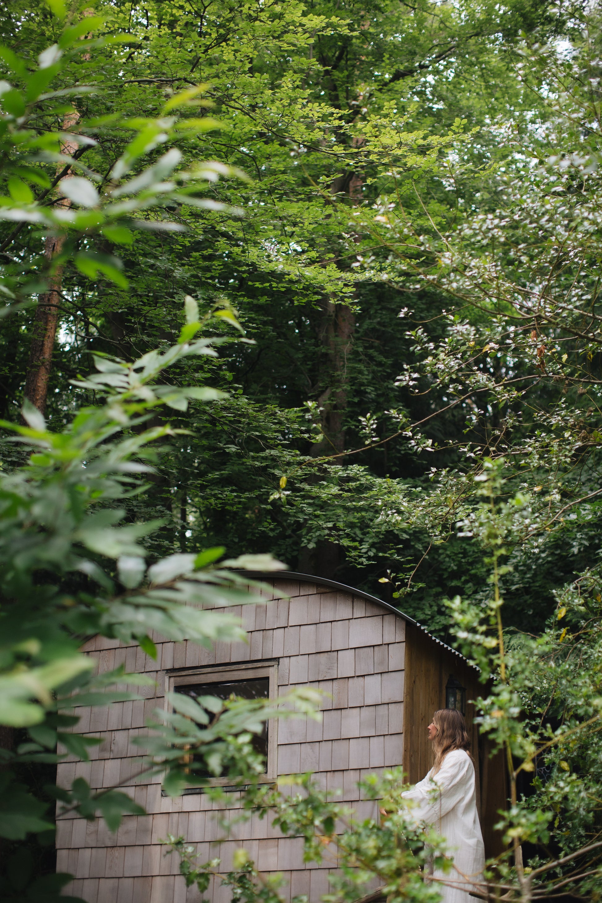 Olivia standing in front of a wooden cabin surrounded by trees